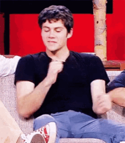 A Young Man Is Sitting On A Couch With His Legs Crossed And Holding A Pen . GIF