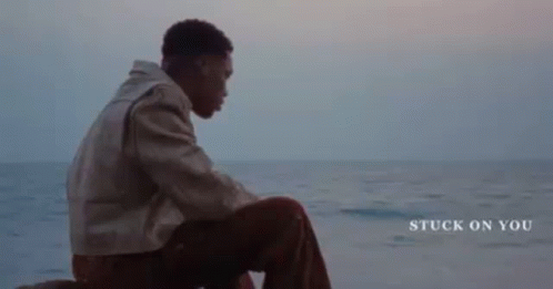 A Young Man Is Sitting On A Rock Near The Ocean . GIF