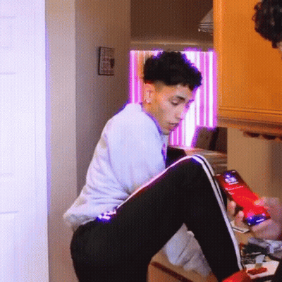 A Young Man Is Sitting On A Table Looking At A Cell Phone . GIF