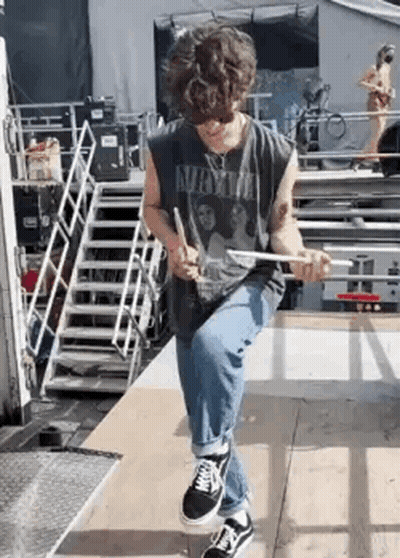 A Young Man Is Sitting On A Wooden Platform Holding A Drum Stick . GIF
