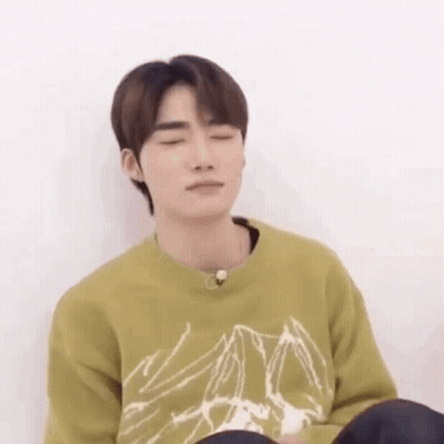 A Young Man Is Sitting On The Floor With His Eyes Closed And Wearing A Green Sweater . GIF