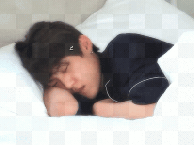 A Young Man Is Sleeping On A Bed With A Headband That Says ` ` N ` ` On It . GIF