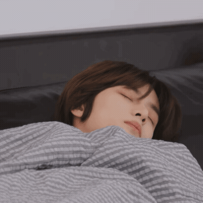 A Young Man Is Sleeping On A Bed With A Striped Blanket GIF