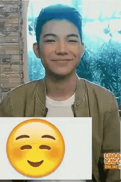 A Young Man Is Smiling And Holding A Picture Of A Smiley Face GIF