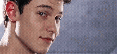 A Young Man Is Smiling And Looking At The Camera With A Blue Background . GIF