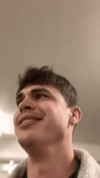 A Young Man Is Smiling And Looking Up At The Ceiling While Wearing A Fur Coat . GIF