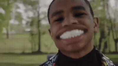 A Young Man Is Smiling And Making A Funny Face In A Park With Trees In The Background . GIF