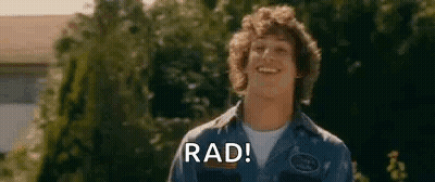 A Young Man Is Smiling And Saying `` Rad '' While Standing In Front Of Trees . GIF