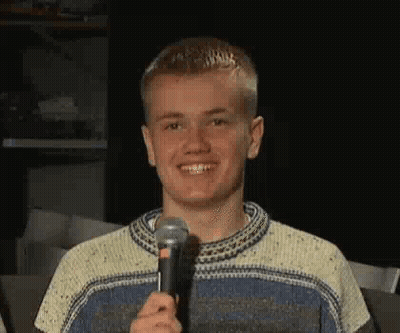 A Young Man Is Smiling While Holding A Microphone In His Hand . GIF