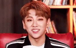 A Young Man Is Smiling While Sitting In A Red Chair . GIF