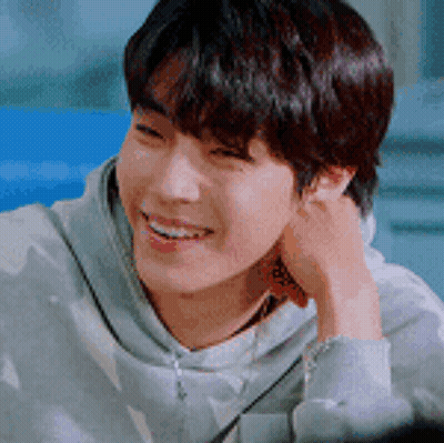 A Young Man Is Smiling With His Hand On His Ear And Wearing A Hoodie . GIF