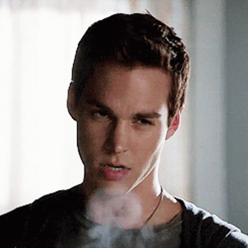 A Young Man Is Smoking A Cigarette And Looking At The Camera With Smoke Coming Out Of His Mouth . GIF