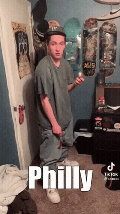 A Young Man Is Standing In A Room With Skateboards On The Wall And Holding A Lighter . GIF