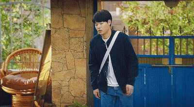 A Young Man Is Standing In Front Of A Blue Fence And A Wicker Chair . GIF
