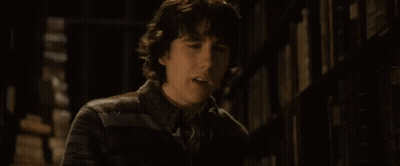 A Young Man Is Standing In Front Of A Bookshelf And Looking At The Camera GIF