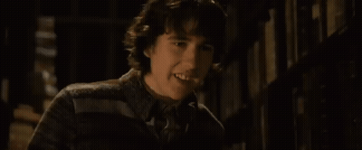 A Young Man Is Standing In Front Of A Bookshelf In A Library . GIF