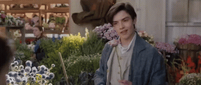 A Young Man Is Standing In Front Of A Bunch Of Flowers In A Flower Shop . GIF