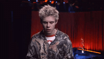 A Young Man Is Standing In Front Of A Red Curtain On A Stage . GIF