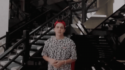 A Young Man Is Standing In Front Of A Set Of Stairs Wearing A Red Hat And A Black And White Shirt . GIF