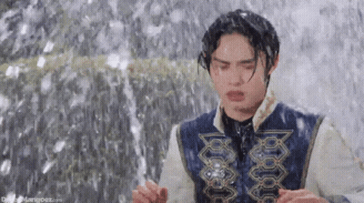 A Young Man Is Standing In Front Of A Waterfall . GIF