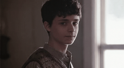 A Young Man Is Standing In Front Of A Window In A Dark Room . GIF