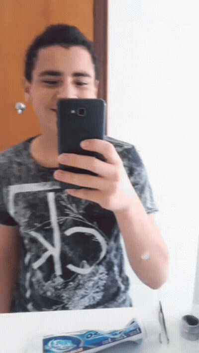 A Young Man Is Taking A Selfie With His Phone In Front Of A Mirror GIF