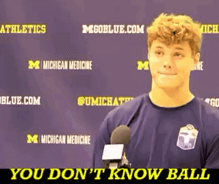 A Young Man Is Talking Into A Microphone In Front Of A Purple Background That Says Michigan Medicine GIF