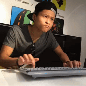 A Young Man Is Typing On A Keyboard In Front Of A Wall That Says Welcome GIF