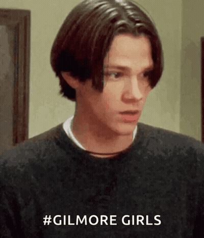 A Young Man Is Wearing A Black Sweater And Has The Hashtag #Gilmore Girls On His Shirt GIF
