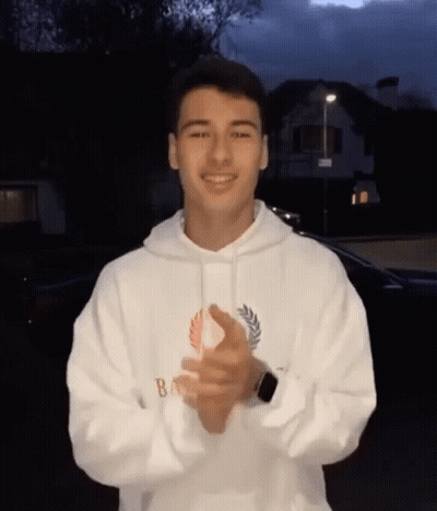 A Young Man Is Wearing A White Hoodie And Clapping His Hands . GIF