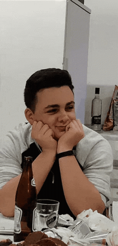 A Young Man Sits At A Table With A Bottle Of Beer And A Glass Of Beer GIF