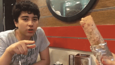 A Young Man Sitting At A Table With A Can Of Soda In Front Of Him And A Sandwich In Front Of Him GIF