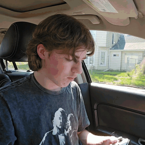 A Young Man Sitting In A Car Wearing A T-Shirt With A Picture Of A Man And Woman On It GIF