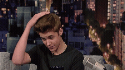 A Young Man Sitting In Front Of A Microphone With His Hand On His Hair GIF