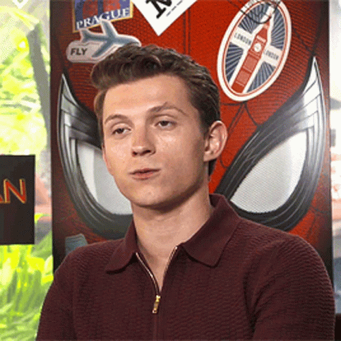 A Young Man Sitting In Front Of A Spider Man Poster With Stickers On It GIF