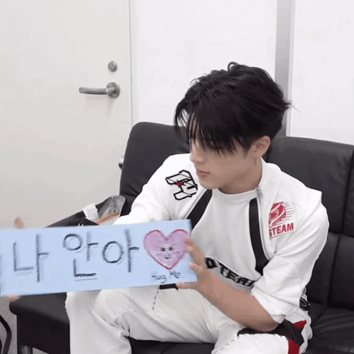 A Young Man Sitting On A Couch Holding A Sign That Says Steam GIF