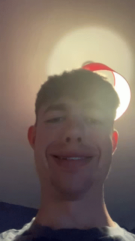 A Young Man Smiles In Front Of A Red Lamp GIF