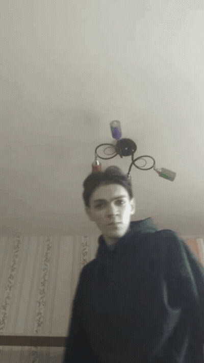 A Young Man Stands In Front Of A Ceiling Light With A Lamp On Top Of His Head GIF