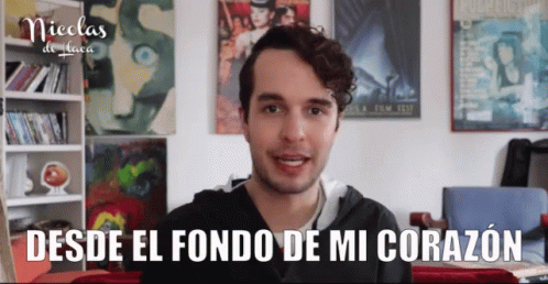 A Young Man Stands In Front Of A Wall With Posters On It And Says Nicolas De Laca GIF
