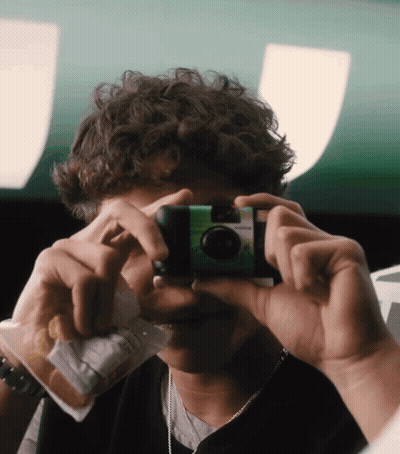 A Young Man Taking A Picture With A Green Camera GIF