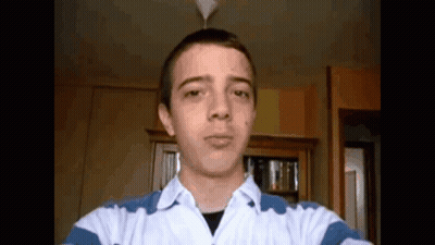 A Young Man Taking A Selfie In A Room With A Bookshelf In The Background GIF