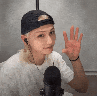 A Young Man Wearing A Baseball Cap And Headphones Is Waving At The Camera . GIF