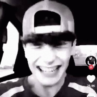 A Young Man Wearing A Baseball Cap Is Smiling In A Car . GIF