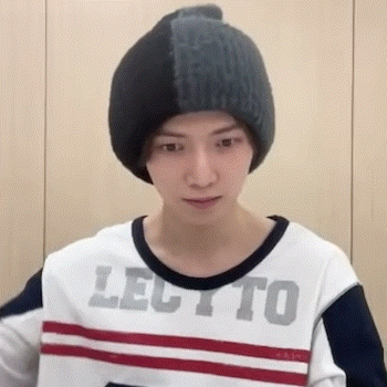 A Young Man Wearing A Beanie And A Striped Shirt Is Standing In Front Of A Wall . GIF