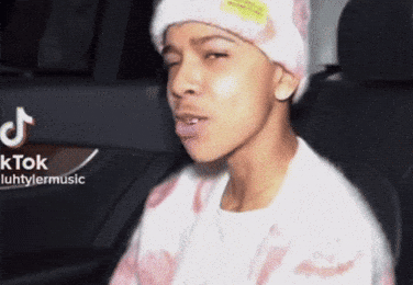 A Young Man Wearing A Beanie And A Sweater Is Sitting In A Car . GIF
