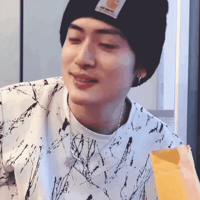 A Young Man Wearing A Black Beanie And A White Shirt Is Eating A Bag Of French Fries . GIF