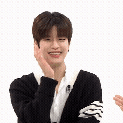 A Young Man Wearing A Black Cardigan And A White Shirt Is Smiling While Holding His Hand To His Face . GIF