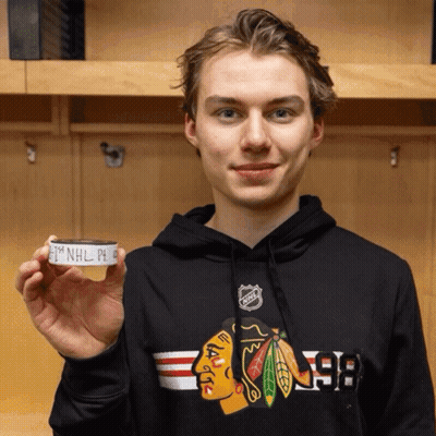 A Young Man Wearing A Black Chicago Blackhawks Sweatshirt Is Holding A Hockey Puck GIF