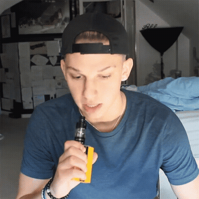 A Young Man Wearing A Black Hat And A Blue Shirt Smoking An Electronic Cigarette GIF