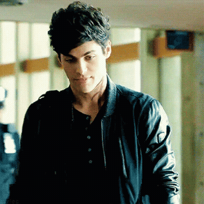 A Young Man Wearing A Black Leather Jacket And A Black Shirt Is Standing In A Hallway . GIF